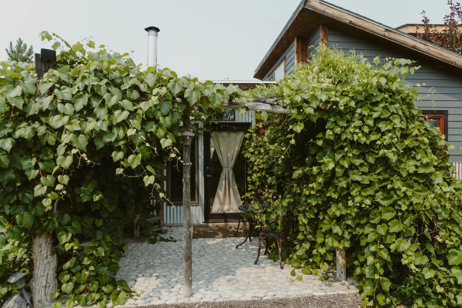 A shaded patio under a grapevine arbor, a bistro table beside the door