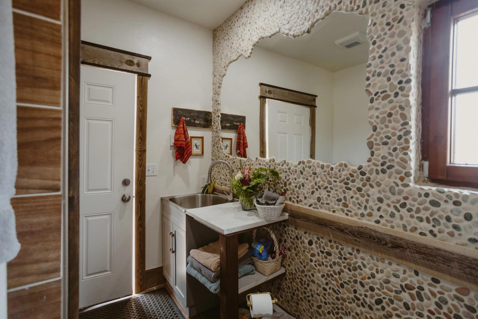 The guest restroom's river-rock mirror wall, sink, and fresh towels