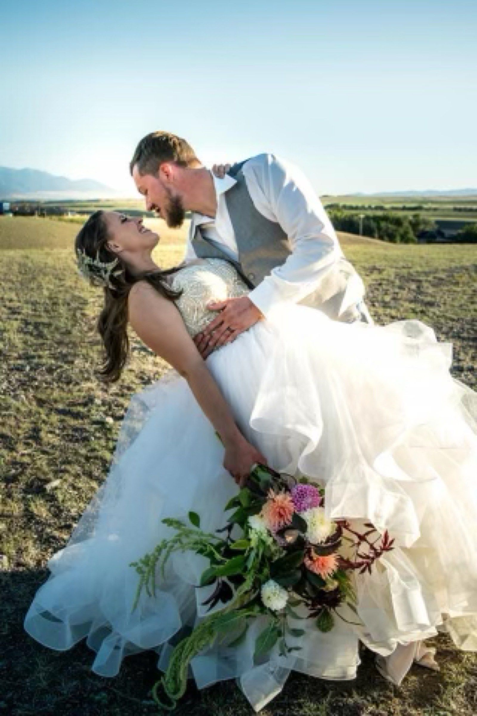A groom dips his bride for a kiss in the field, her dahlia bouquet trailing below