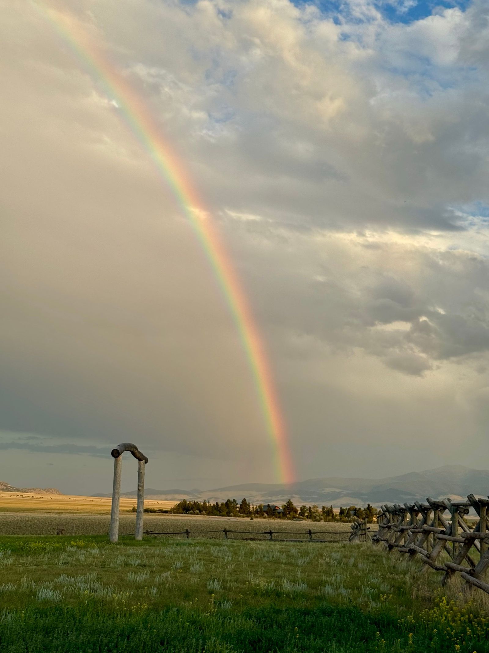 A rainbow arcing over the log ceremony arch in the meadow, storm clouds over the valley and the jackleg fence