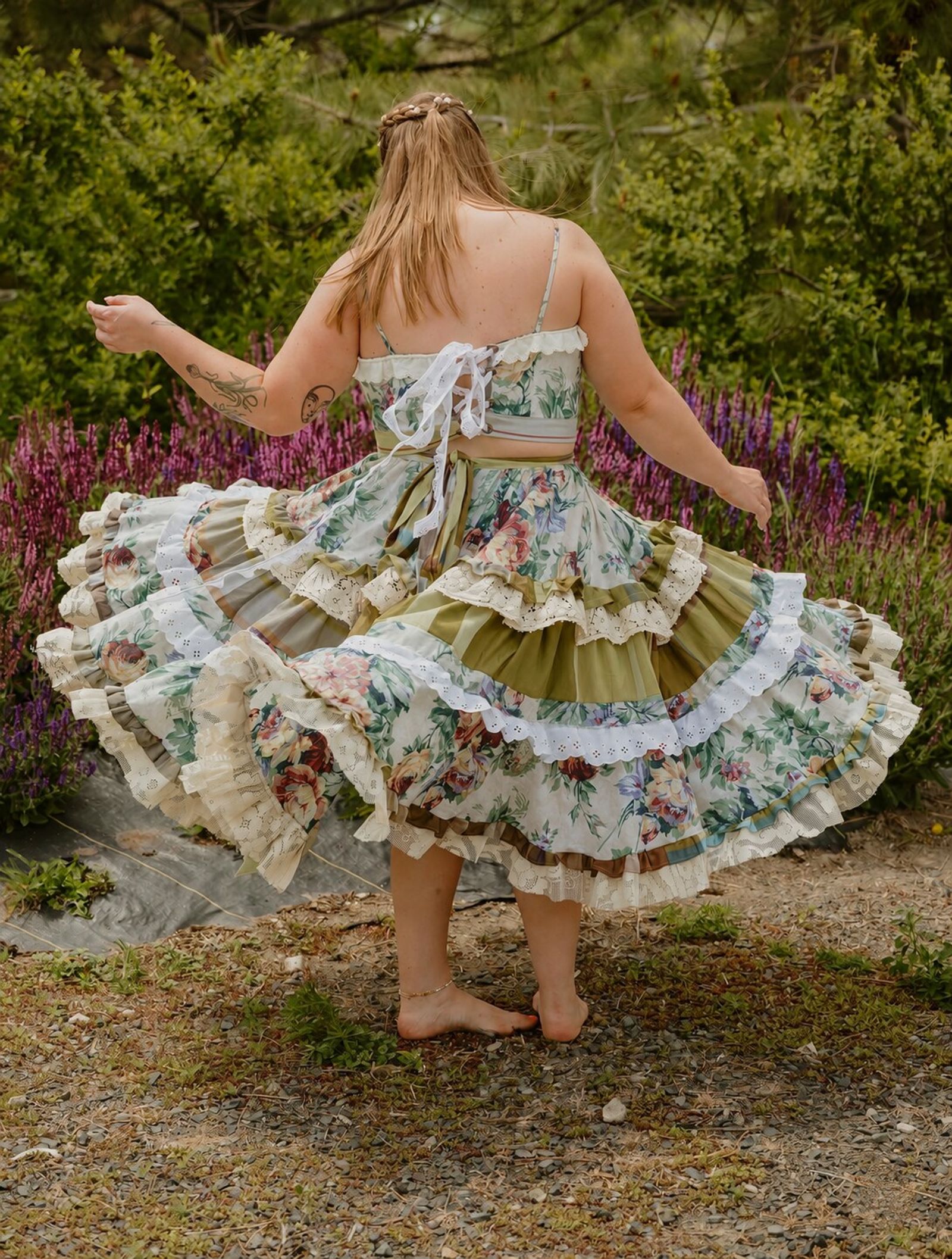 Twirling barefoot in a ruffled floral dress beside the purple blooms in the garden