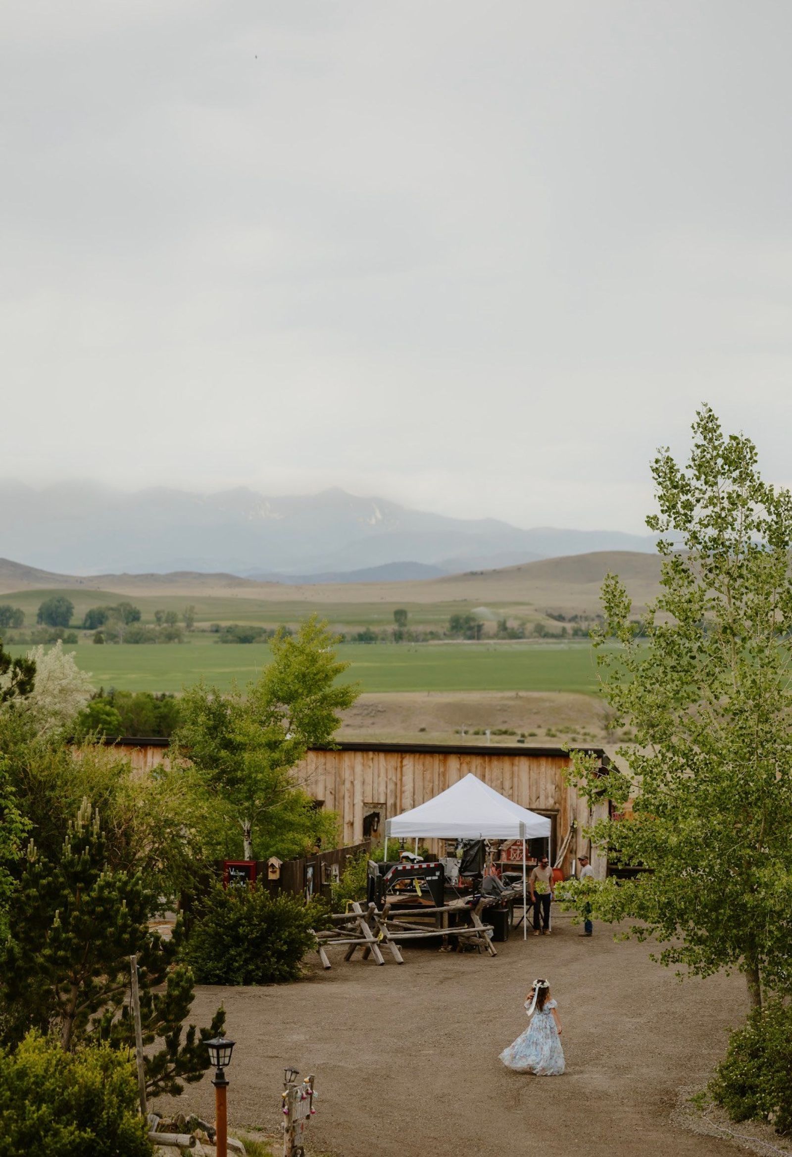 A flower girl twirling across the yard as the band sets up, mountains under low clouds beyond