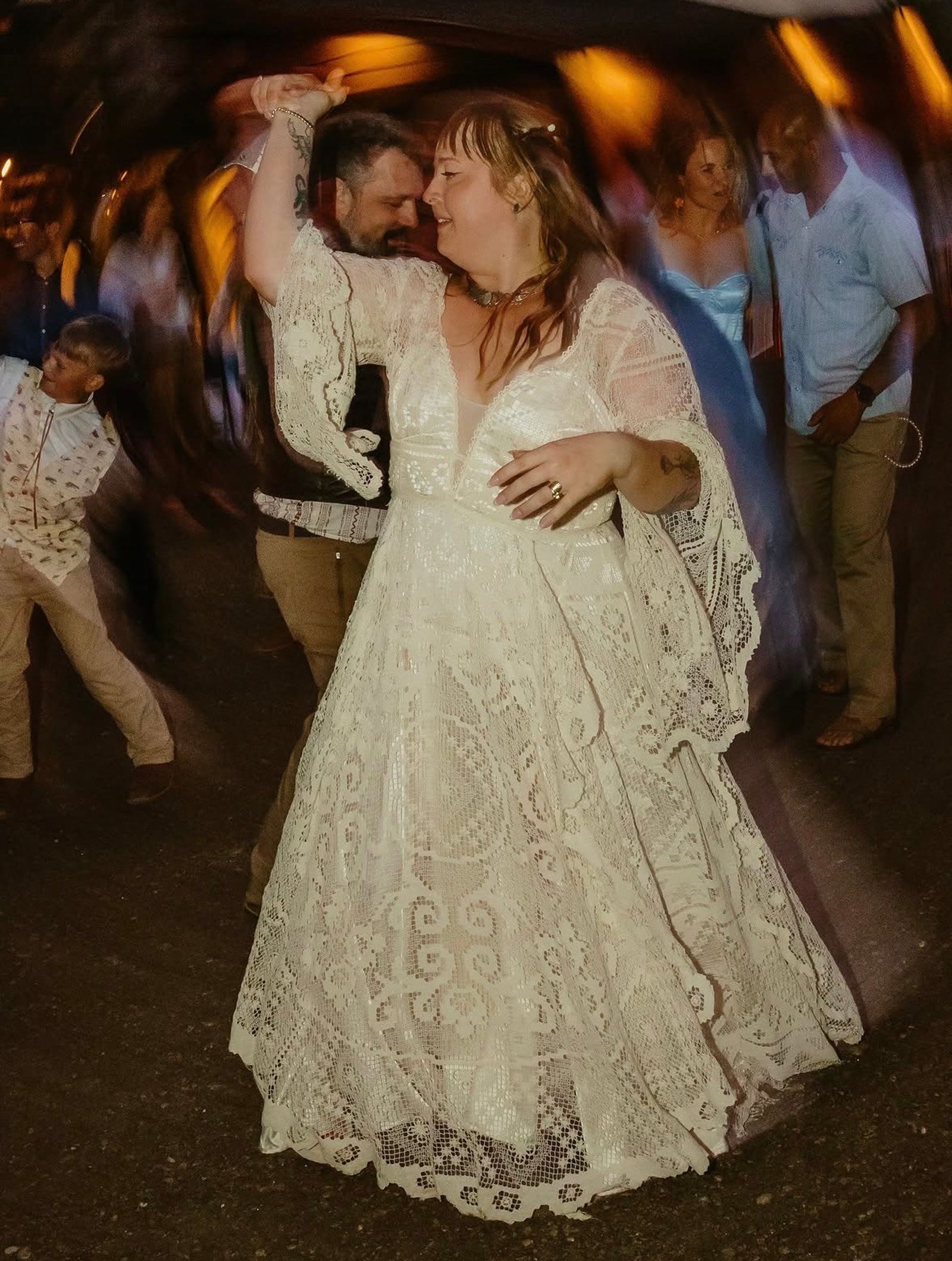 A bride in lace dancing under the lights as the party carries on around her