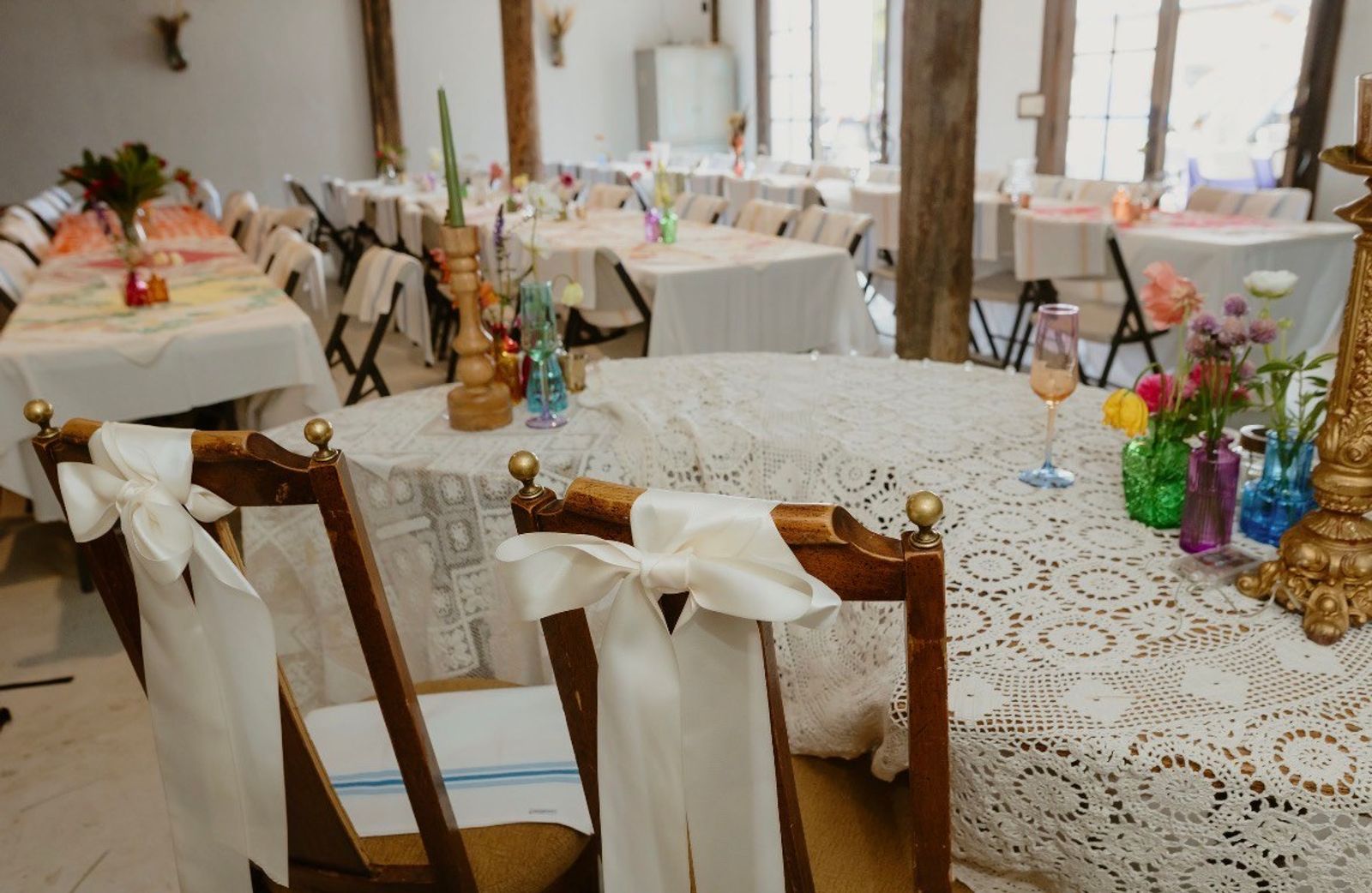 The sweetheart table inside the Bourbon Barn - two wooden chairs tied with white satin bows, a crochet lace tablecloth, and bud vases of garden flowers