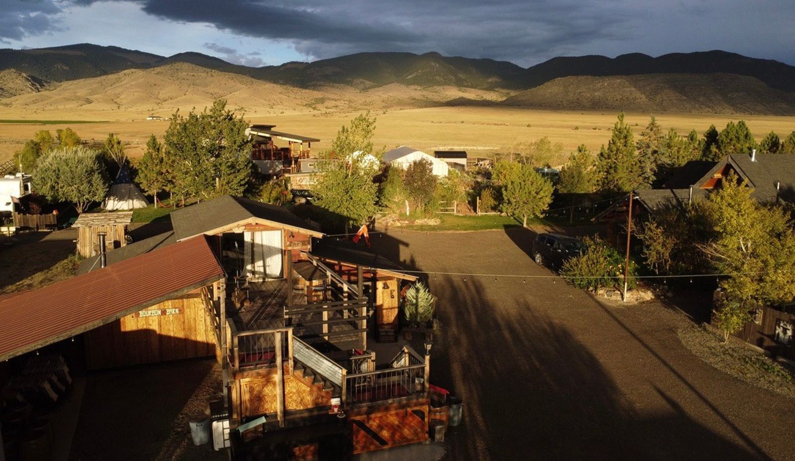 The Bourbon Barn and its deck in late golden light, the farm lane running out toward the valley and the mountains