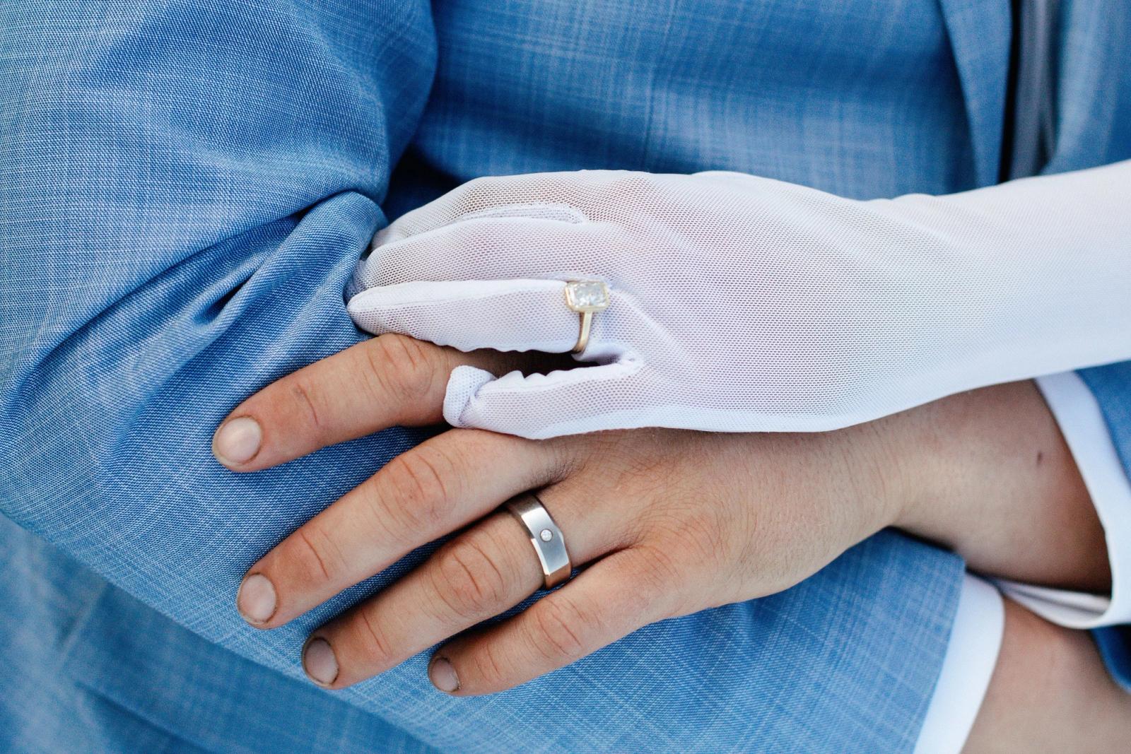 Close-up of the rings: her gloved hand over his, both wedding bands catching the light