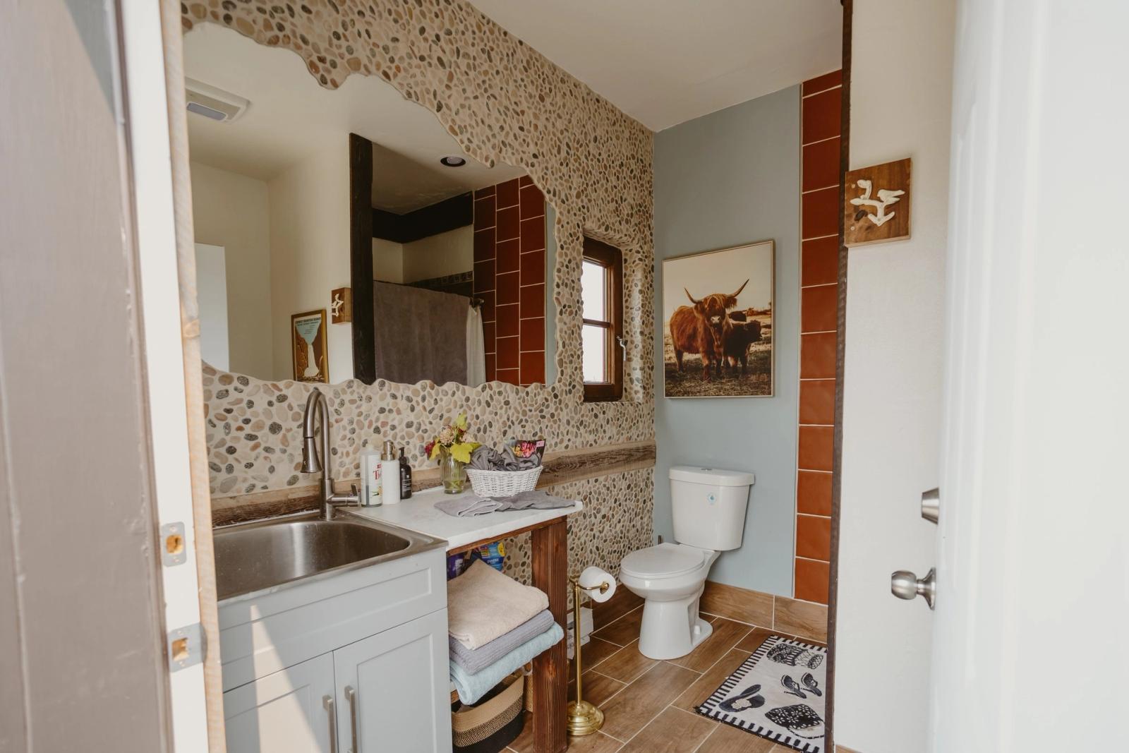 Inside the guest restroom - a river-rock mirror wall, fresh flowers by the sink, and a Highland cow print