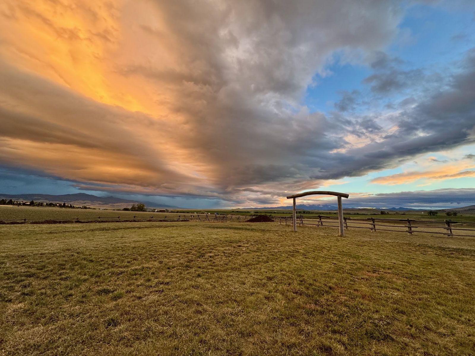 Sunset clouds glowing over the meadow, the log arch small on the horizon