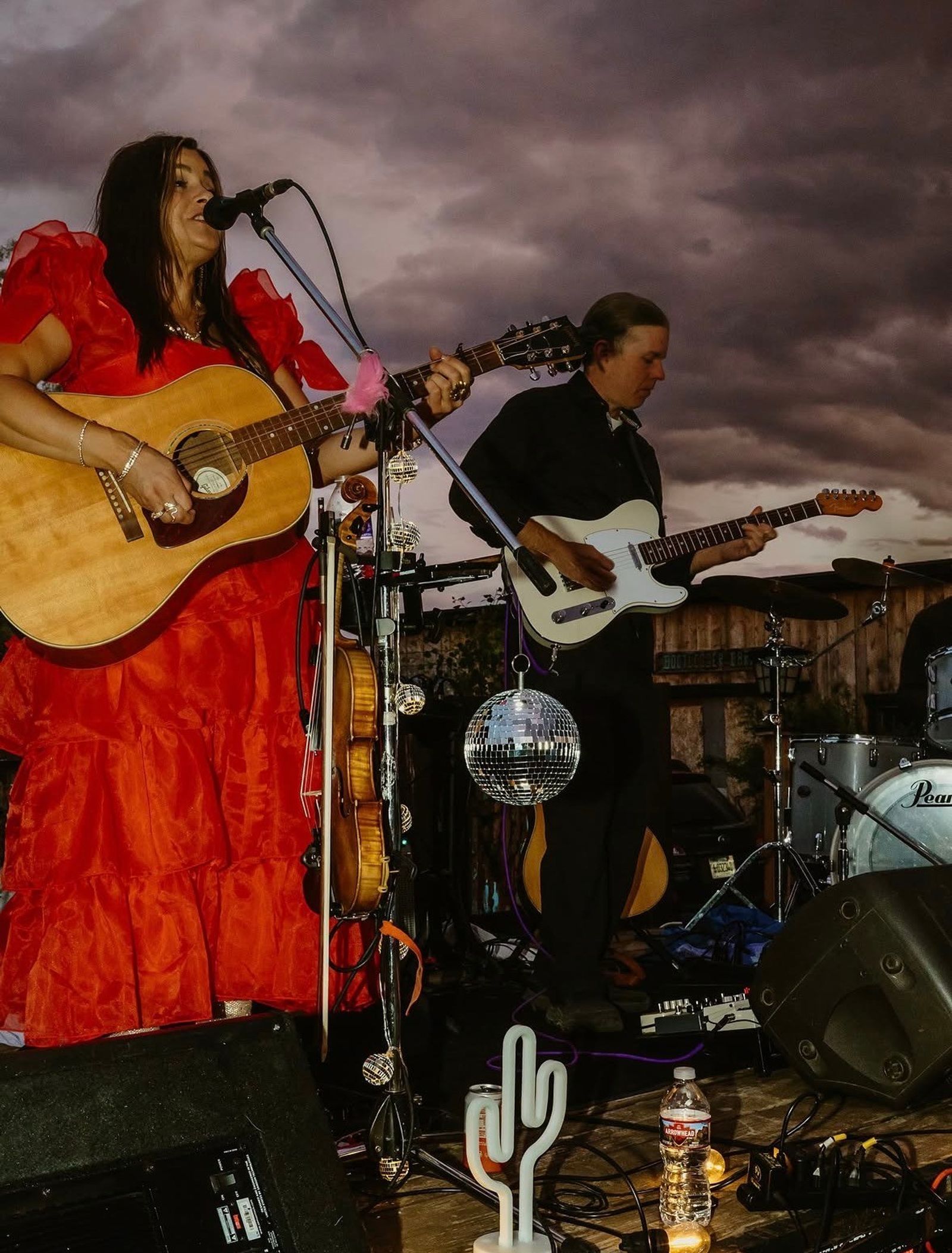 The band plays on under a purple storm sky, a disco ball hanging from the mic stand
