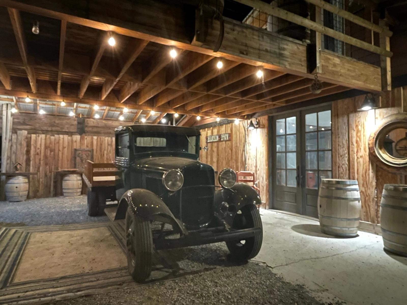 The 1932 Ford parked inside the Bourbon Barn at night under Edison lights, whiskey barrels by the French doors