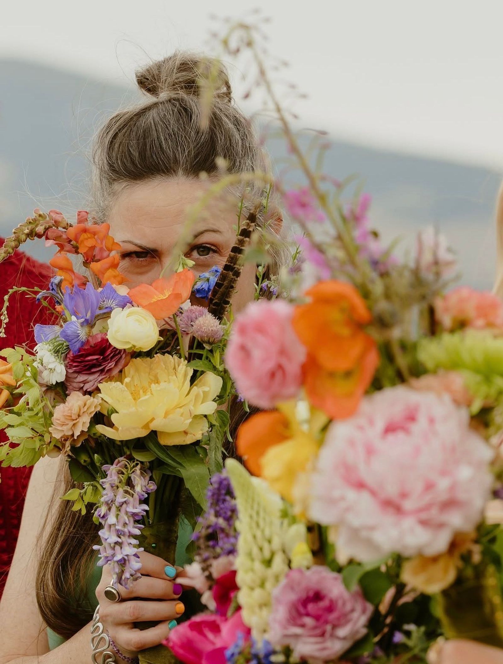 A guest peeking over a bright bouquet of peonies, poppies, and wisteria