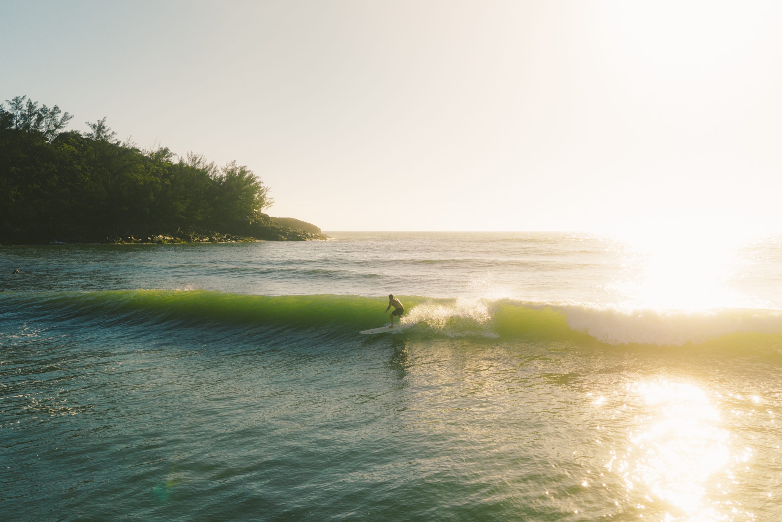 Surfista en una ola verde con el sol de frente en Ferrugem