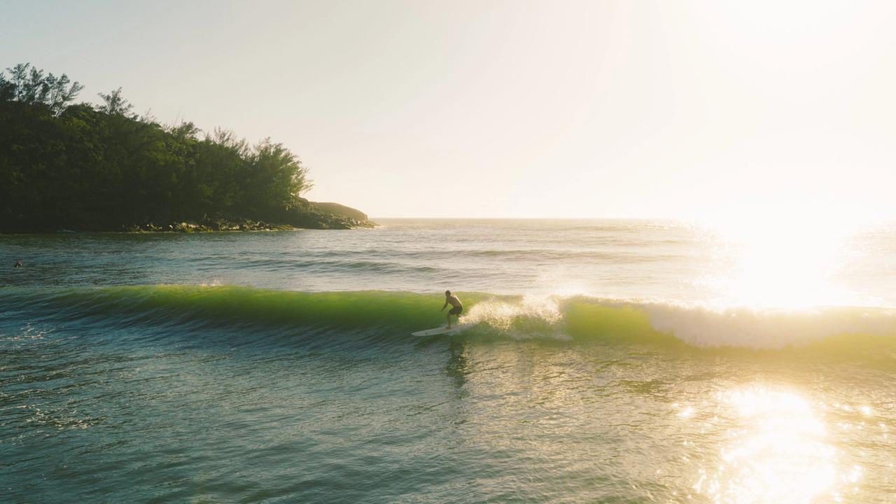 Surfista en una ola verde con el sol de frente en Ferrugem