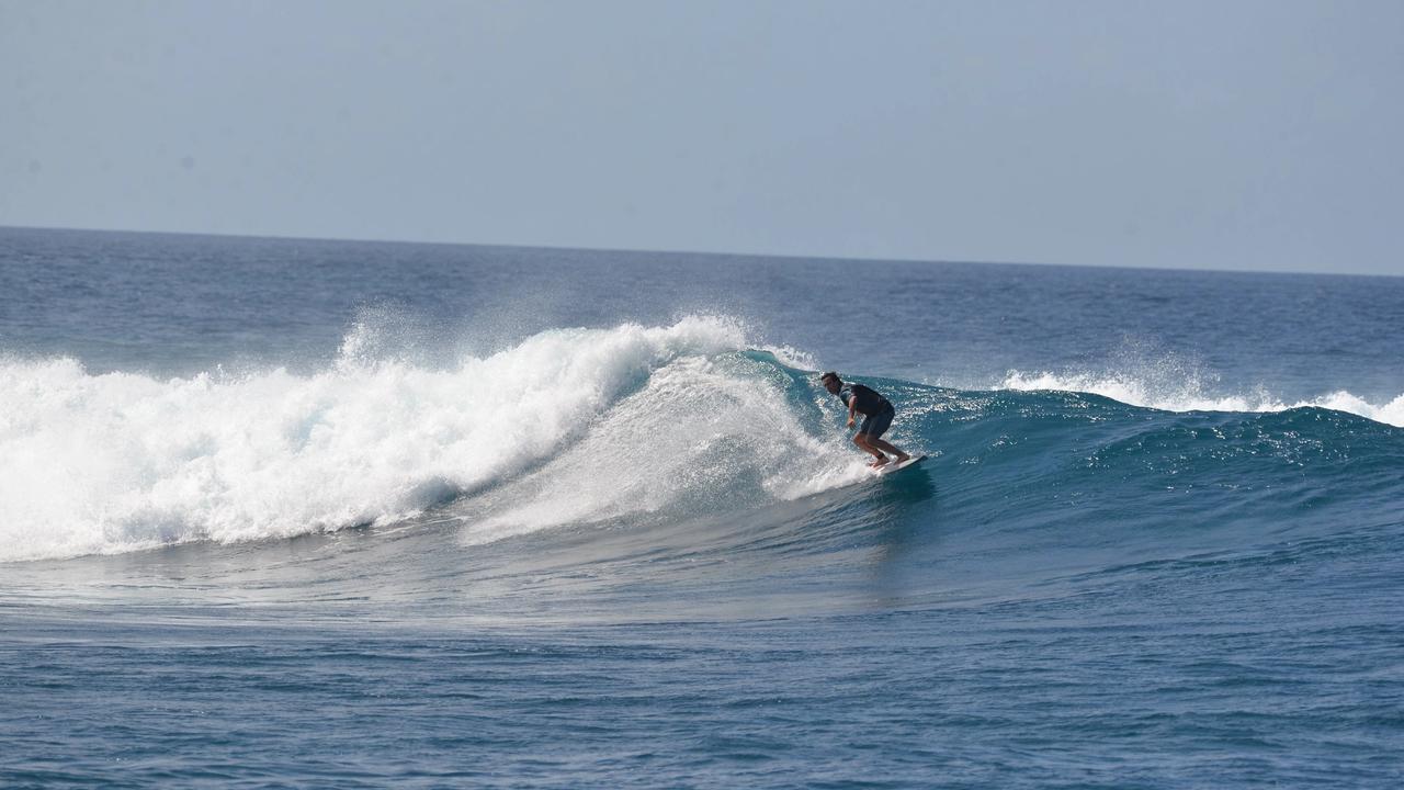 Surfista en una ola que rompe sobre el arrecife en Maldivas, con agua azul y cielo despejado