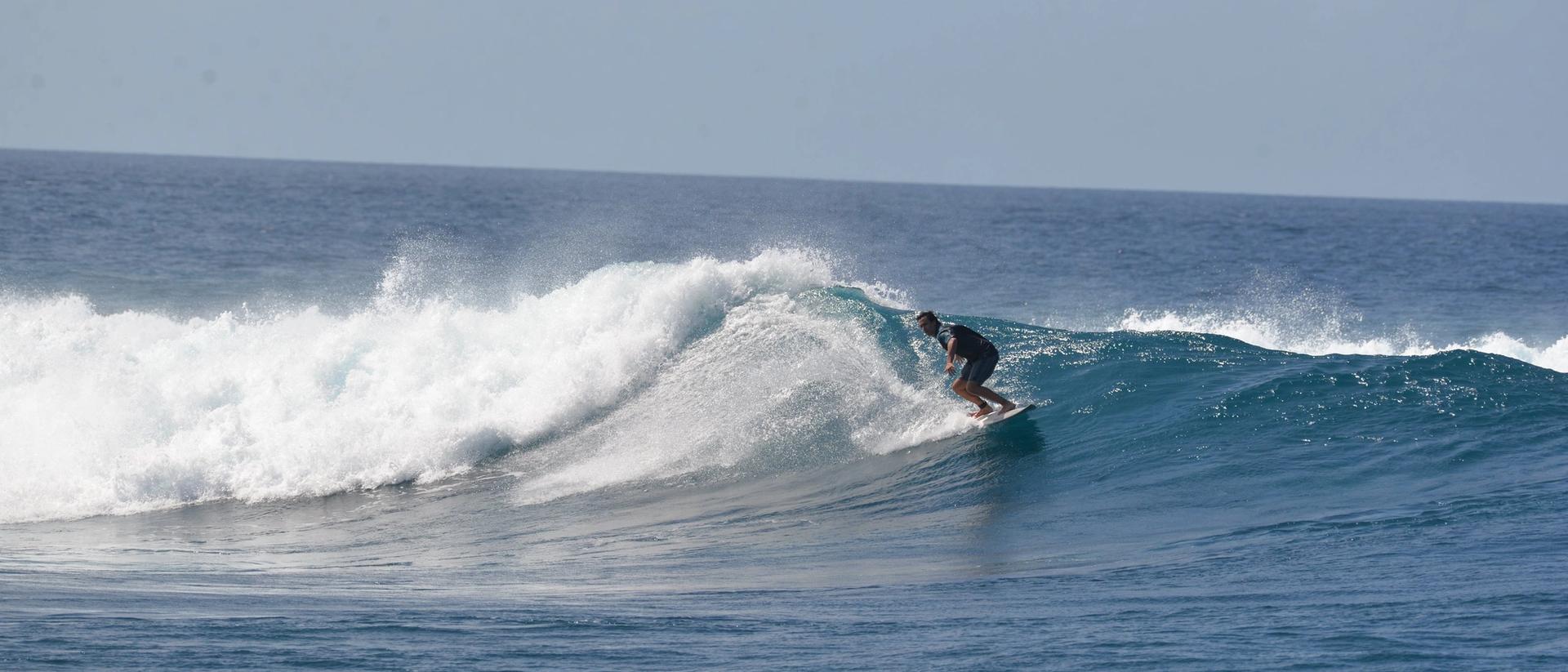 Surfista en una ola que rompe sobre el arrecife en Maldivas, con agua azul y cielo despejado