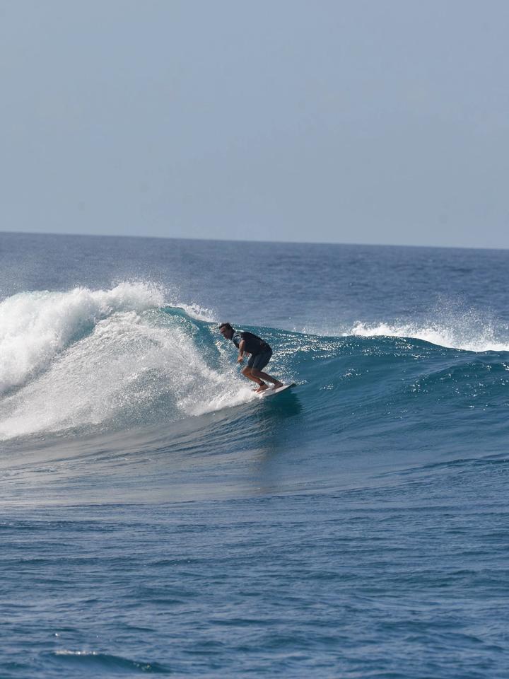 Surfista en una ola que rompe sobre el arrecife en Maldivas, con agua azul y cielo despejado
