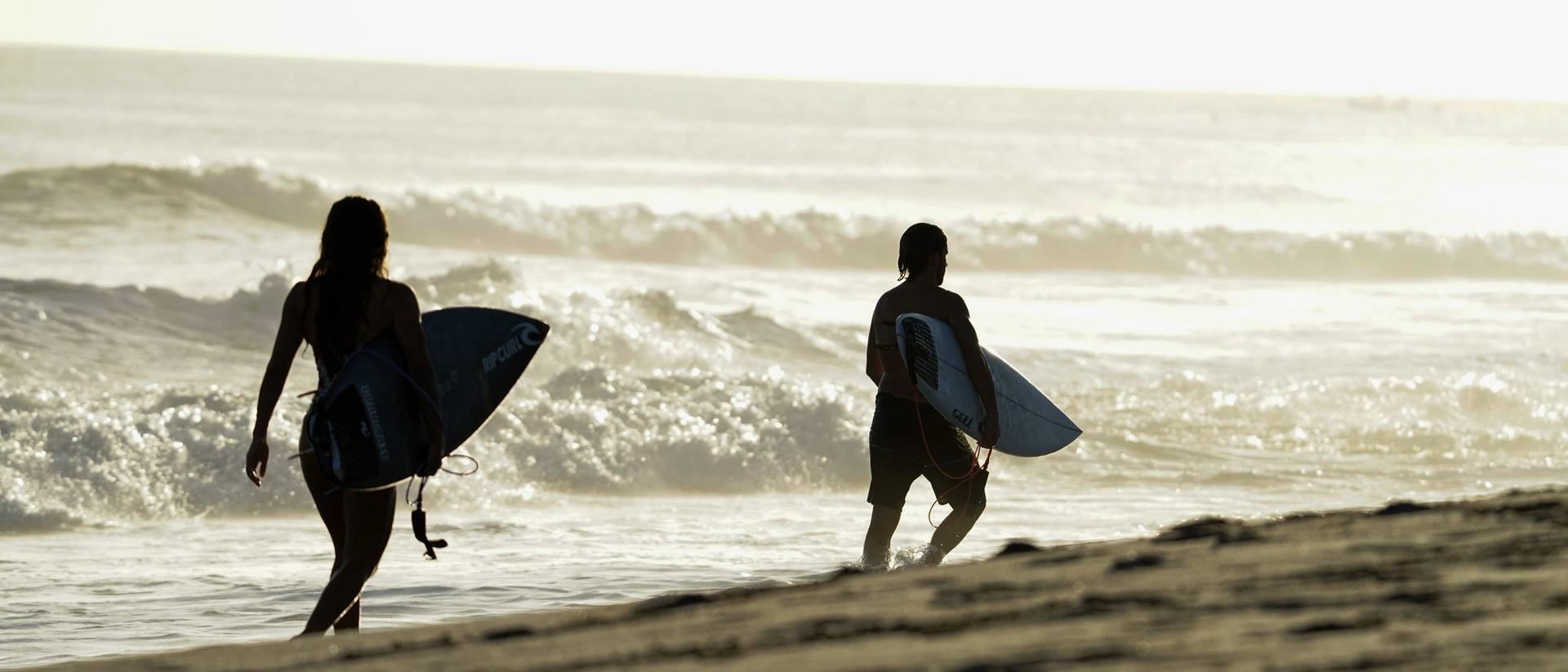 Dos surfistas con sus tablas caminando por la orilla al atardecer en Nicaragua