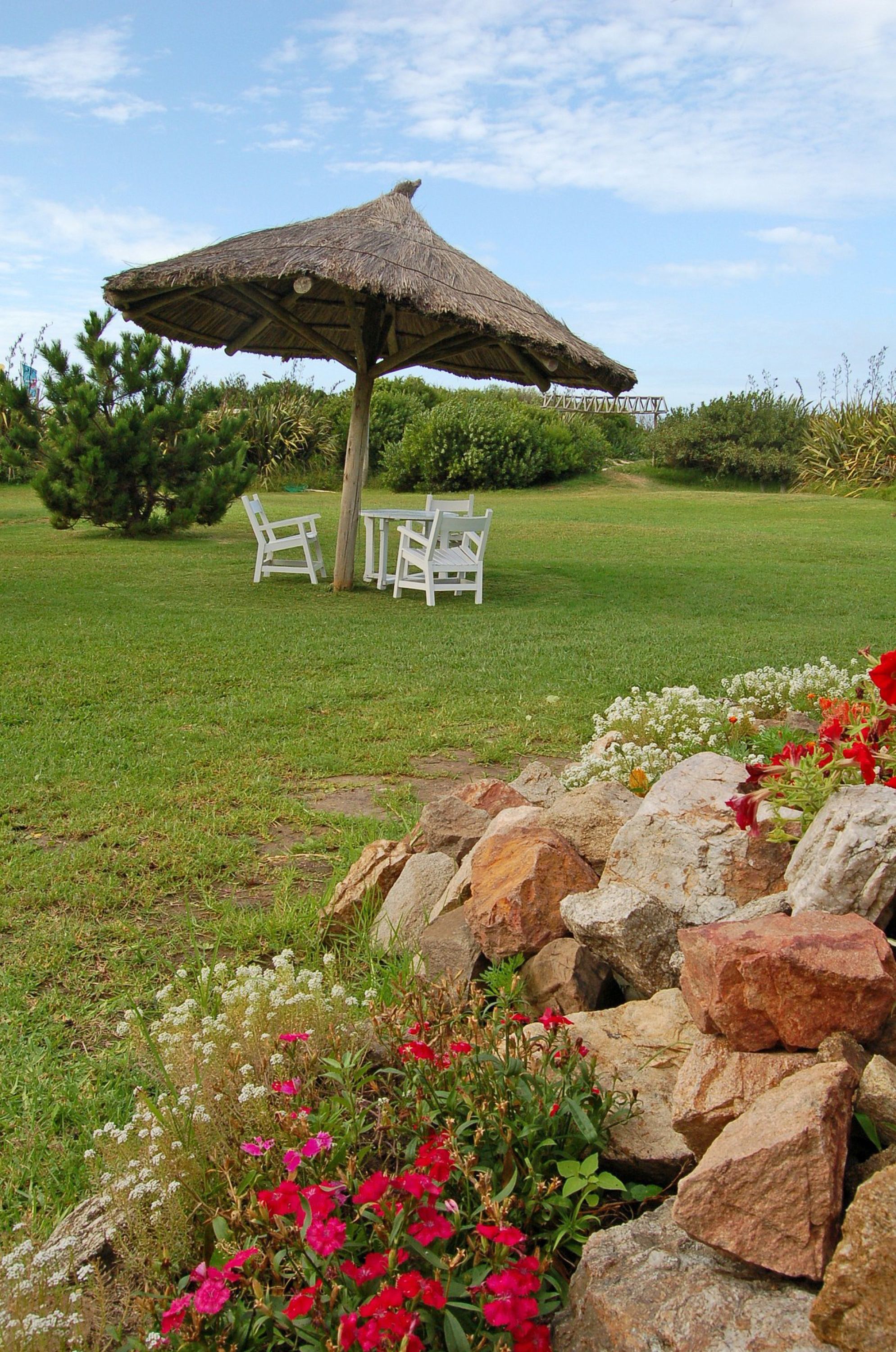 Jardín con sombrilla de paja y vista al mar en Portobello Suites