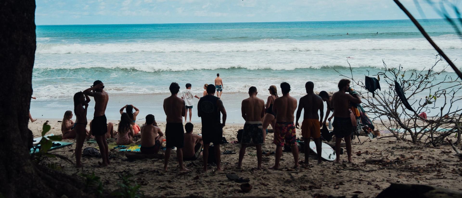 Grupo de viajeros de Mango mirando el mar desde la playa, entre árboles