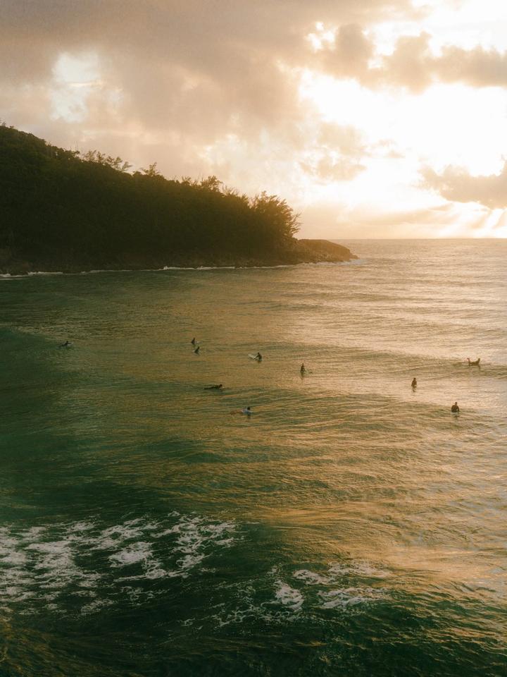 Vista aérea al atardecer de una playa del sur de Brasil, con surfistas esperando olas junto a un morro con vegetación