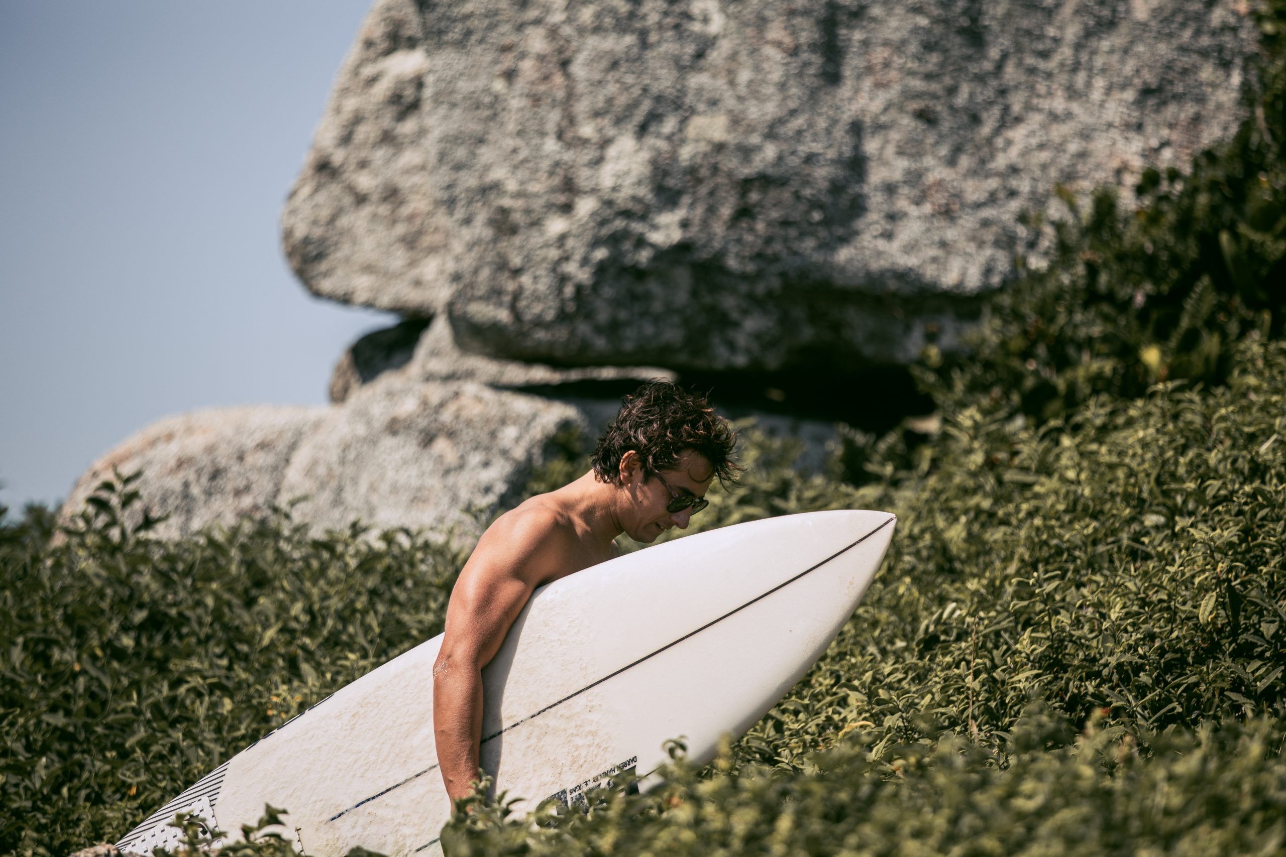 Surfista con su tabla entre la vegetación camino a la playa