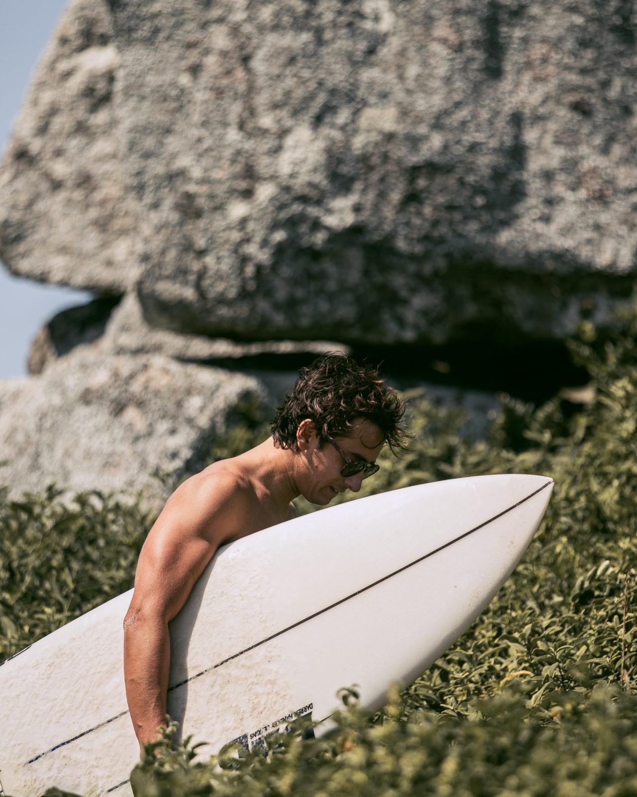 Surfista con su tabla entre la vegetación camino a la playa