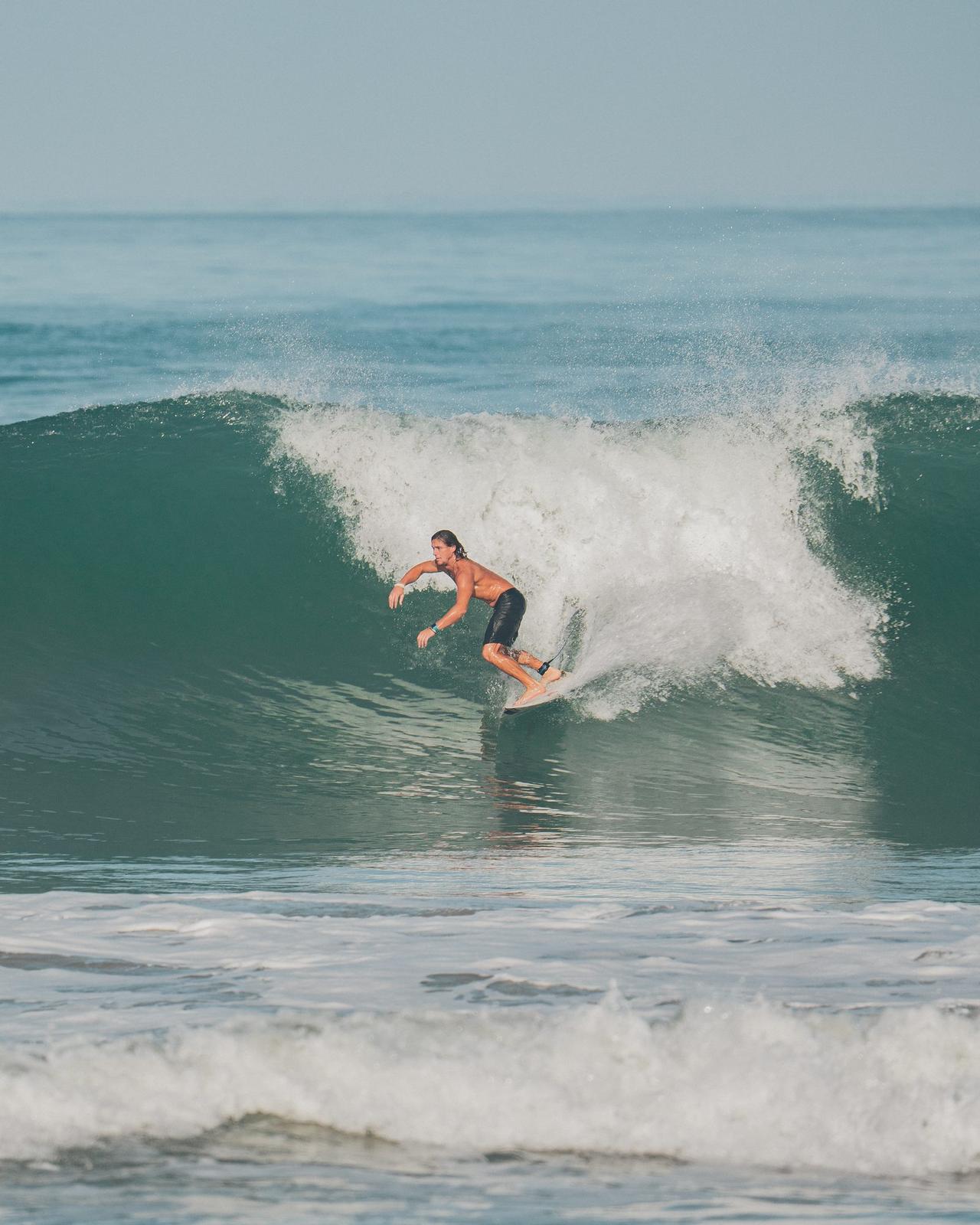 Surfista en la pared de la ola, con la espuma rompiendo atrás