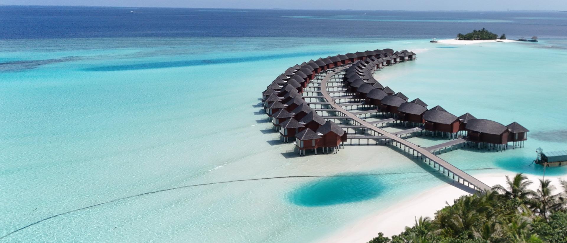 Vista aérea de villas sobre el agua turquesa y una playa con palmeras en Maldivas