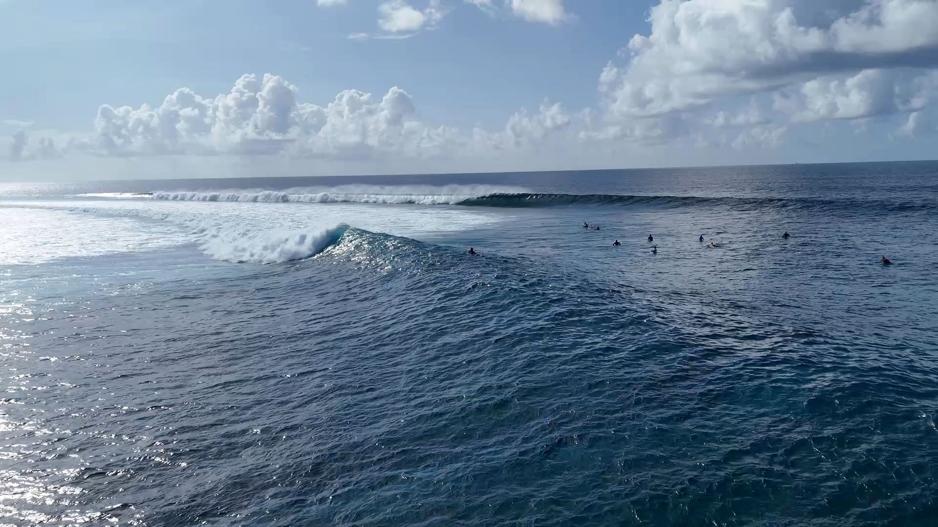 Olas rompiendo en el mar abierto, con surfistas esperando en la línea