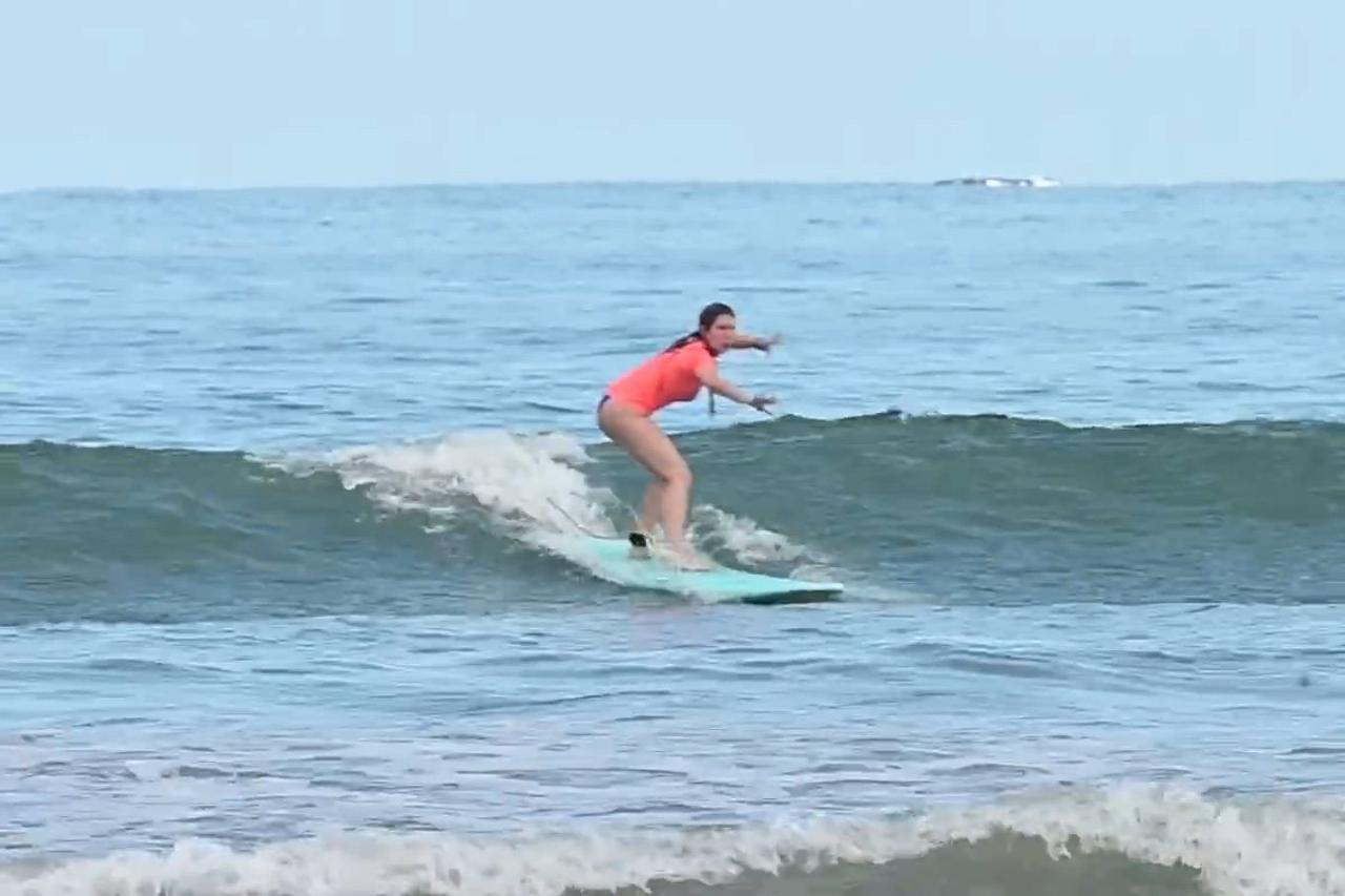 Principiante parada en su tabla corriendo una ola en Costa Rica