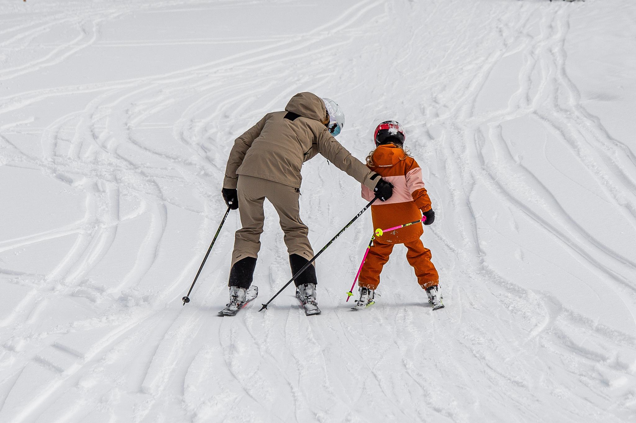 Ein Skifahrer schiebt ein Kind an
