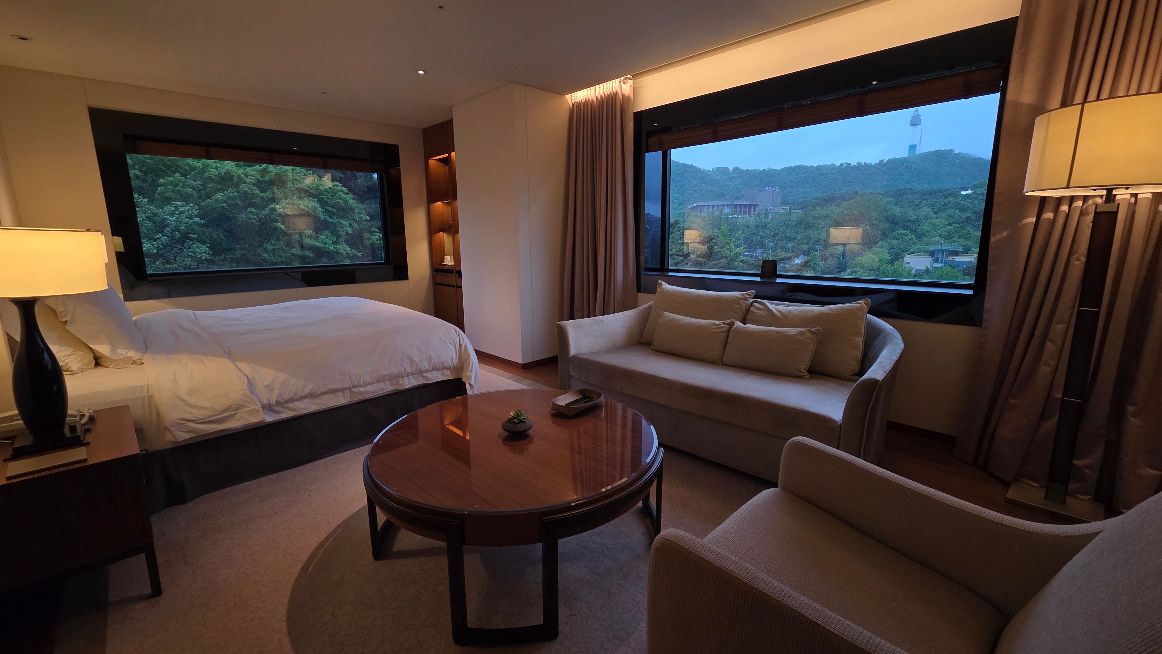 A Seoul hotel room with windows, green view, and evening light.