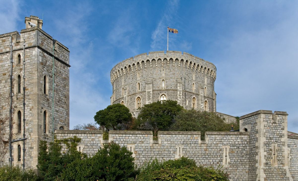 Windsor Castle's Round Tower and walls under a blue sky, with a flag flying from the tower.