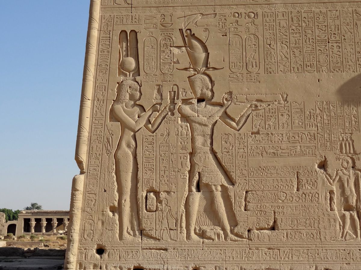 Sandstone temple wall carved with a queen and a king among hieroglyphs.