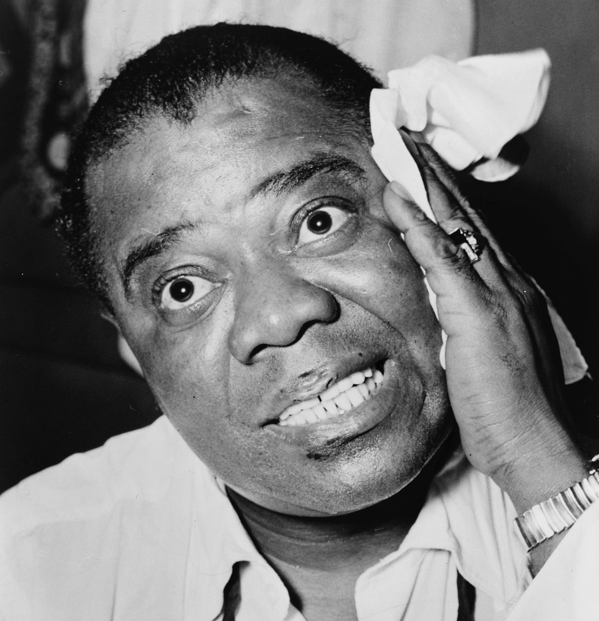 Louis Armstrong in a black-and-white 1953 portrait, wiping his forehead with a white handkerchief.