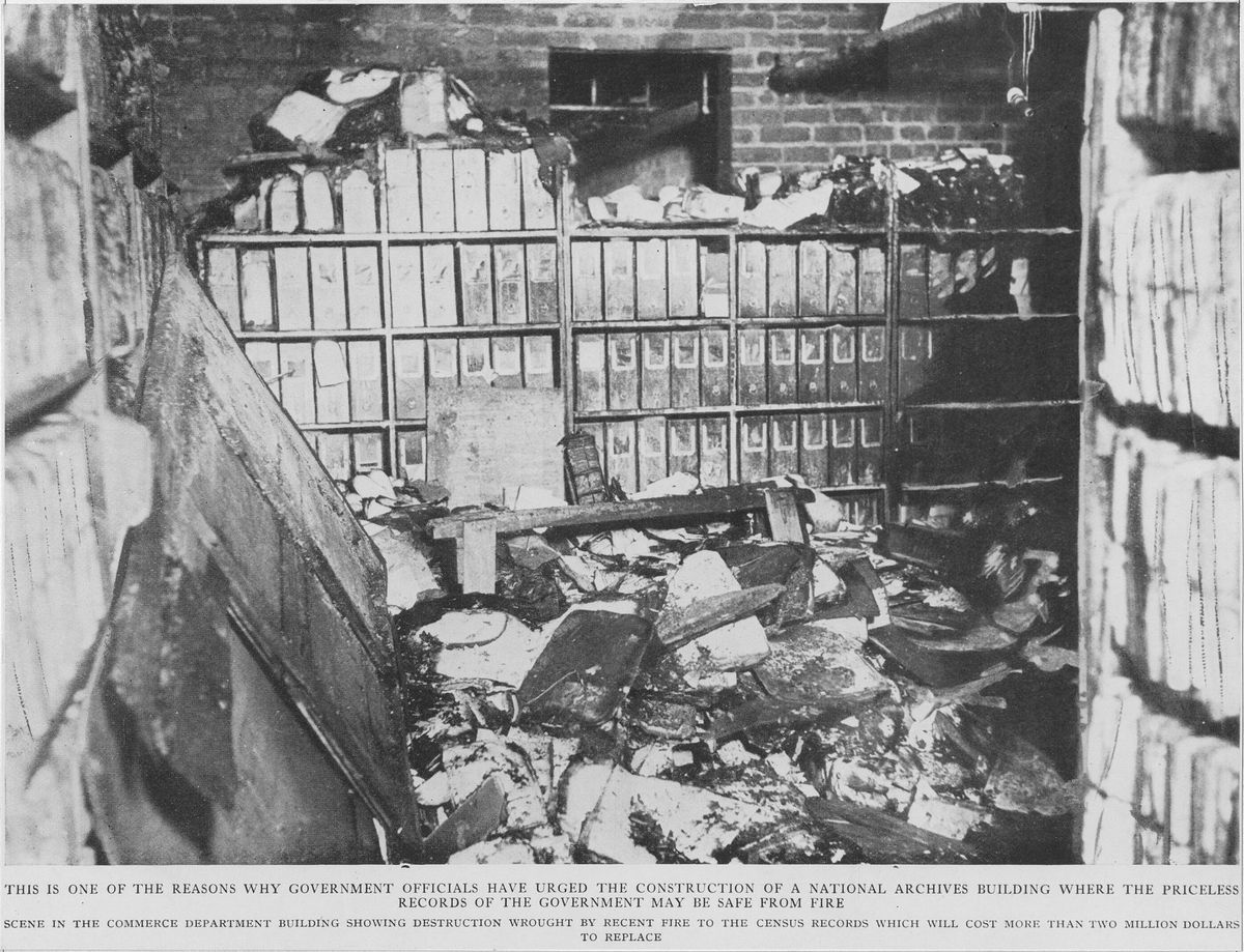 A burned records storage room with charred shelves of bound volumes and a heap of debris and damaged paper on the floor.