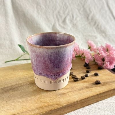 Handgjord keramikmugg i färgen Dimrosa med lila toner och texten “KAFFE KÄRRING”. Muggen står på en träbräda tillsammans med kaffebönor och rosa blommor i mjukt naturligt ljus.