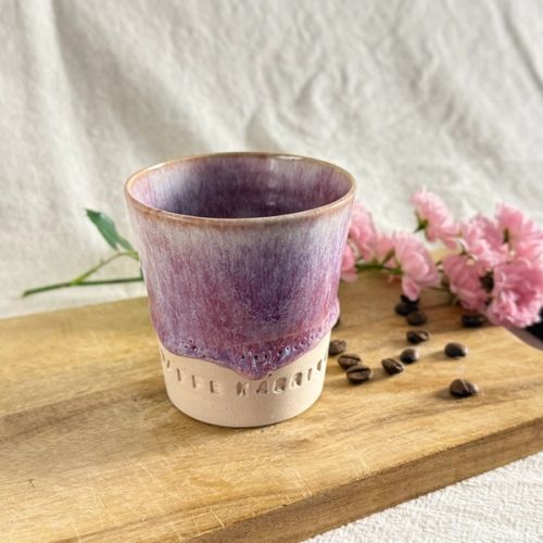 Handgjord keramikmugg i färgen Dimrosa med lila toner och texten “KAFFE KÄRRING”. Muggen står på en träbräda tillsammans med kaffebönor och rosa blommor i mjukt naturligt ljus.