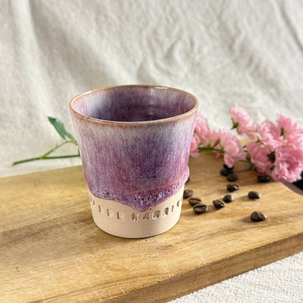 Handgjord keramikmugg i färgen Dimrosa med lila toner och texten “KAFFE KÄRRING”. Muggen står på en träbräda tillsammans med kaffebönor och rosa blommor i mjukt naturligt ljus.