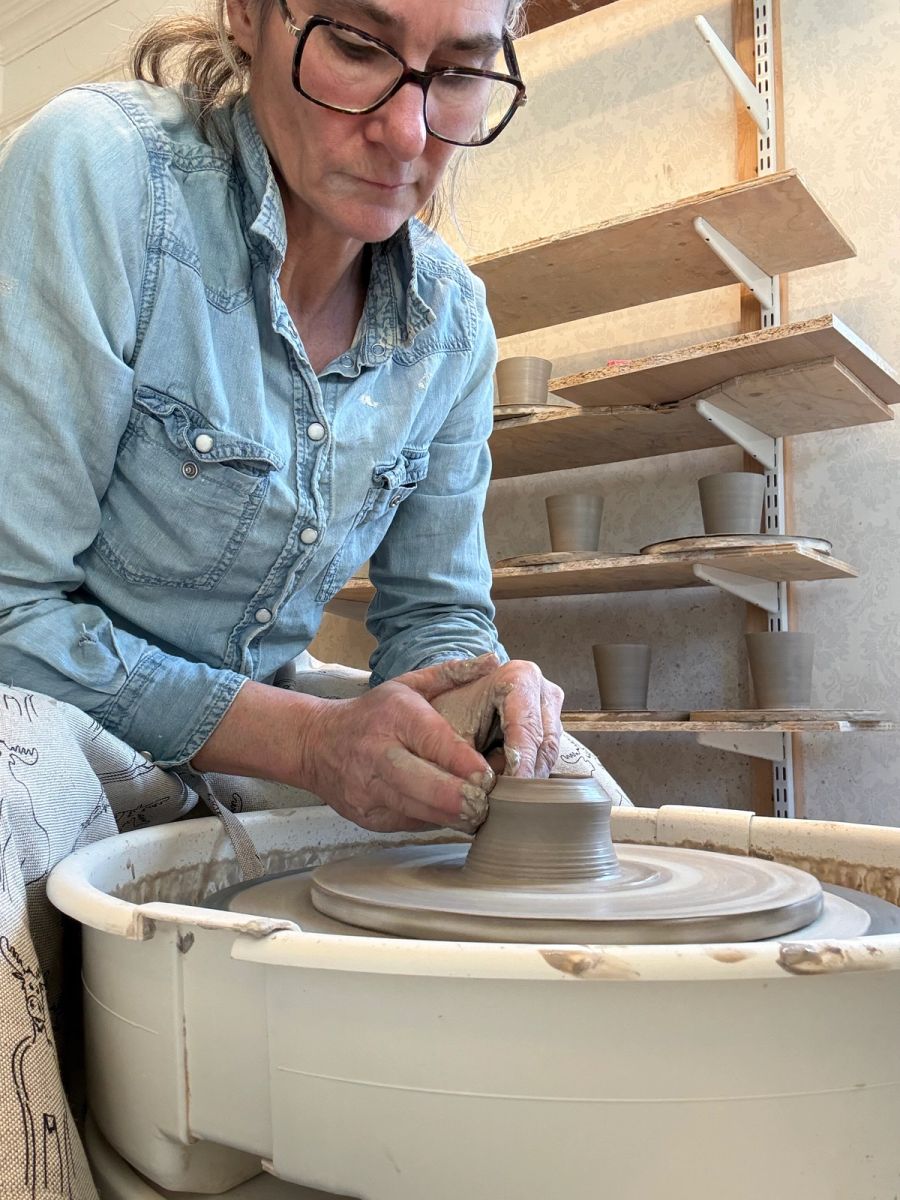 Åsa drejar en lerform med händerna vid drejskivan i sin keramikverkstad.