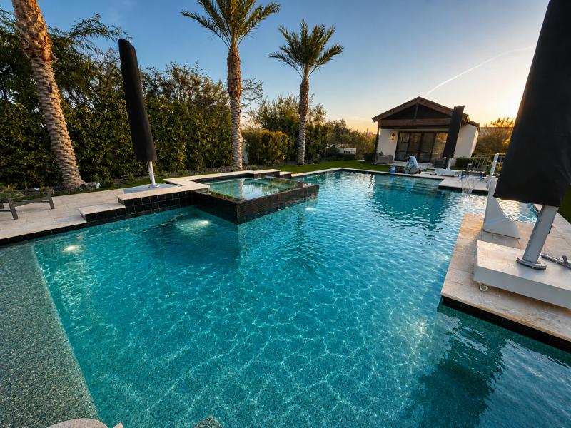 A wide-angle photo of a freshly replastered swimming pool with smooth white plaster finish, sparkling blue water filling in, set in a Scottsdale, AZ backyard with clean pool deck and desert landscaping under bright sunlight.