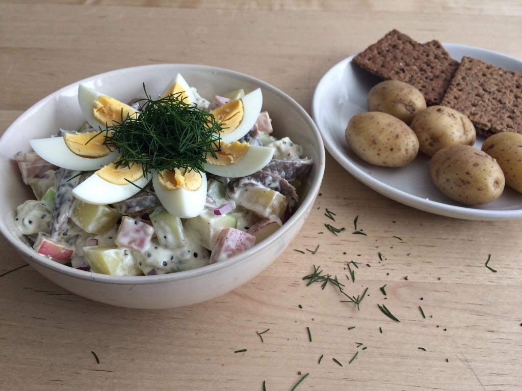 White bowl of Swedish pickled herring salad with potato, apple, and dill, topped with quartered hard-boiled eggs
