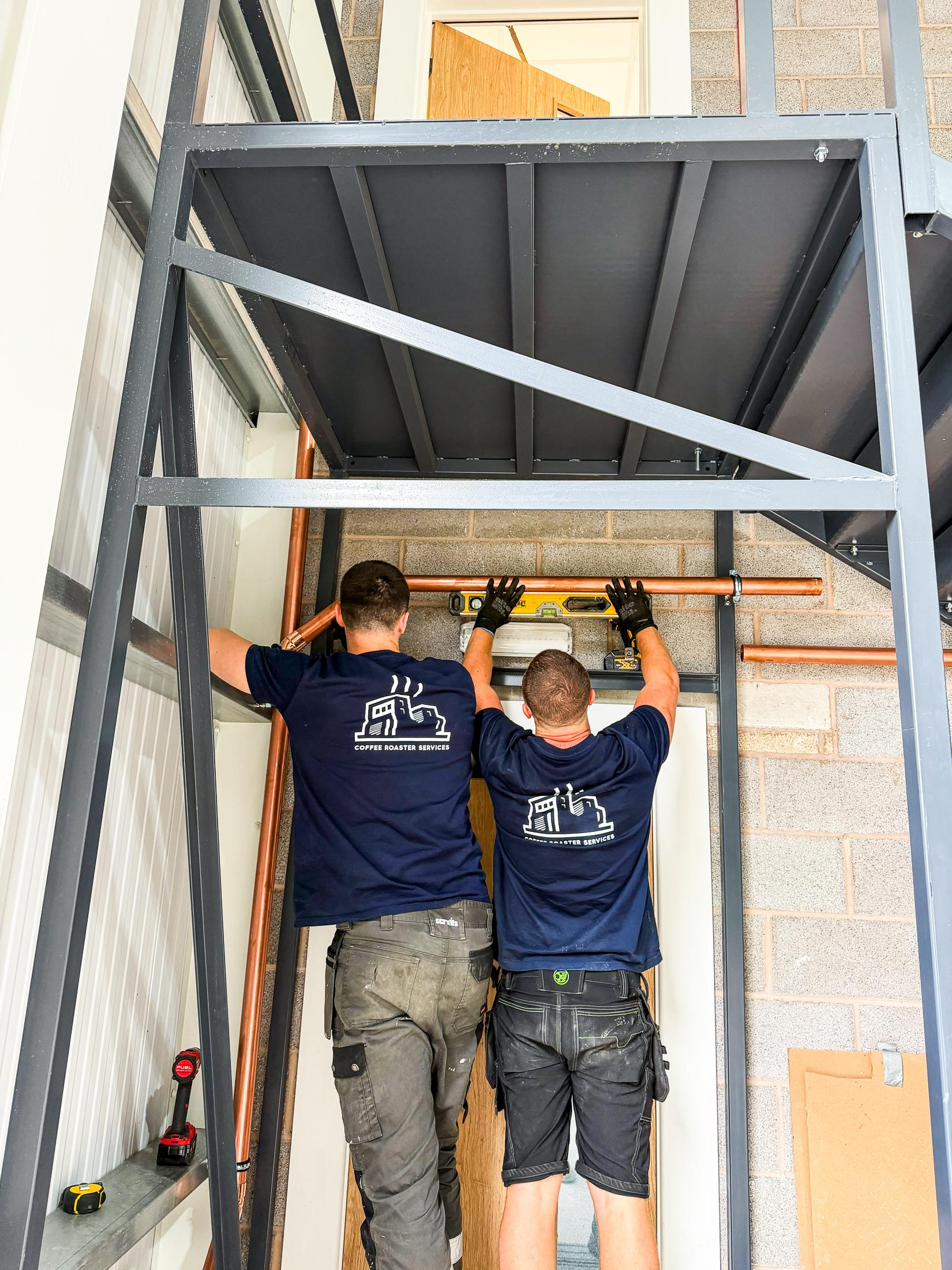 Two engineers fitting pipework during a coffee roaster installation