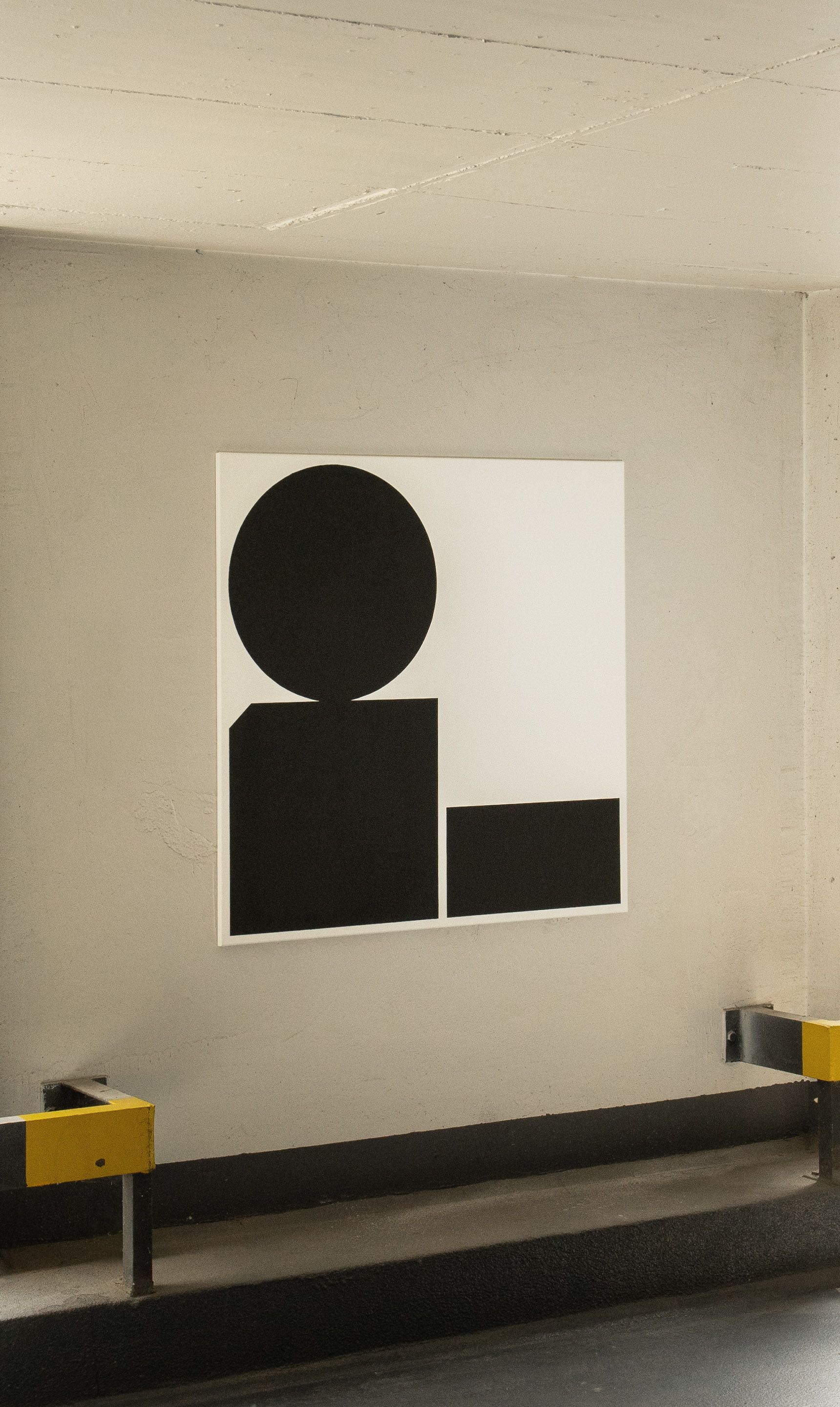 Black and white abstract acrylic painting on canvas with geometric shapes — two rectangles and a balancing circle — displayed in a parking garage.