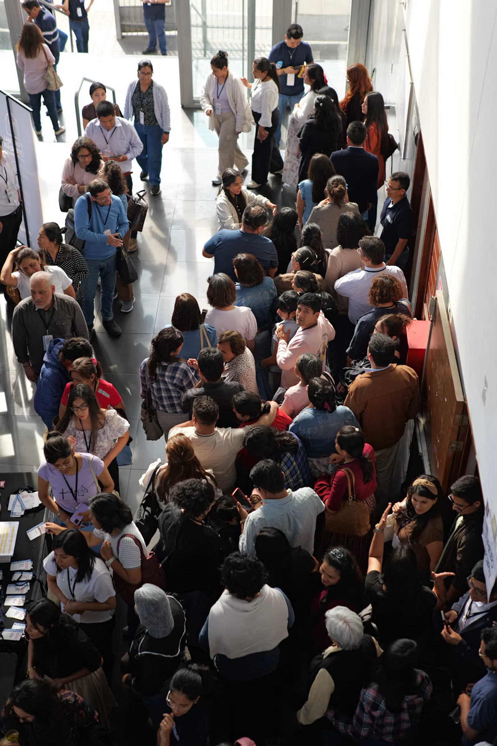 A busy conference lobby seen from above, attendees with lanyards queuing and talking.