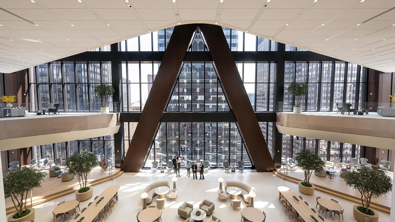 A tall atrium with an A-shaped frame and floor-to-ceiling windows above a seating area.
