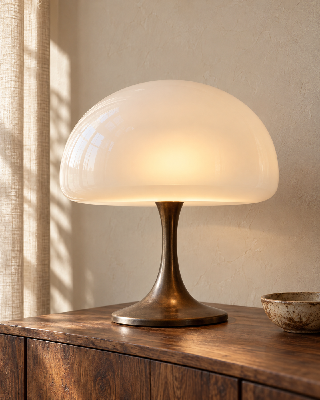 Glowing opal dome lamp on a walnut sideboard, with a linen curtain.
