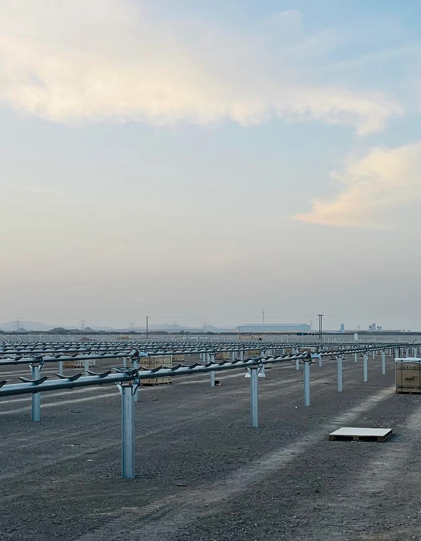Rows of solar panel mounting structures at a construction site with Jinko Solar module crates and mountains at dusk