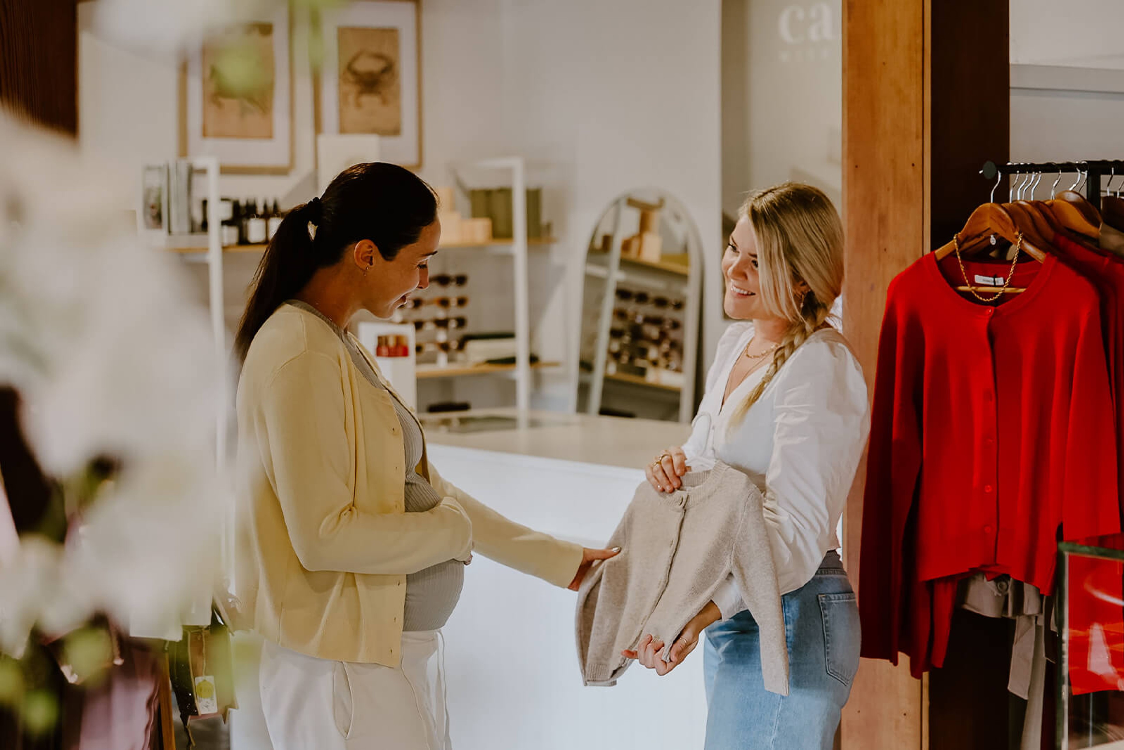 A woman offering a cardigan to a pregnant lady at a store