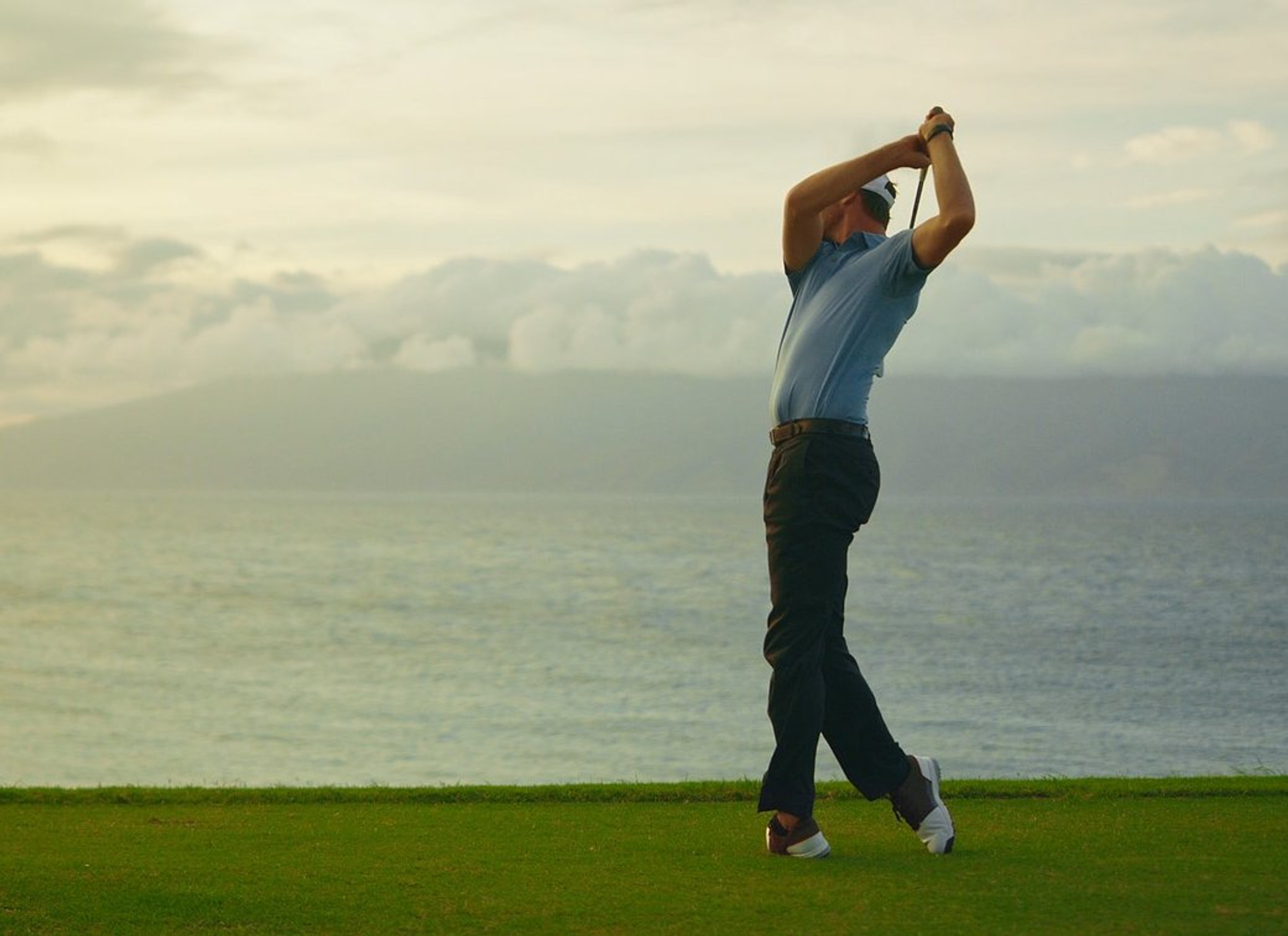 Golfer swinging on a green above the sea